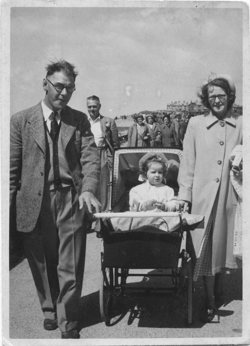 Helen, a toddler, in a pram, with her mother and father on either side